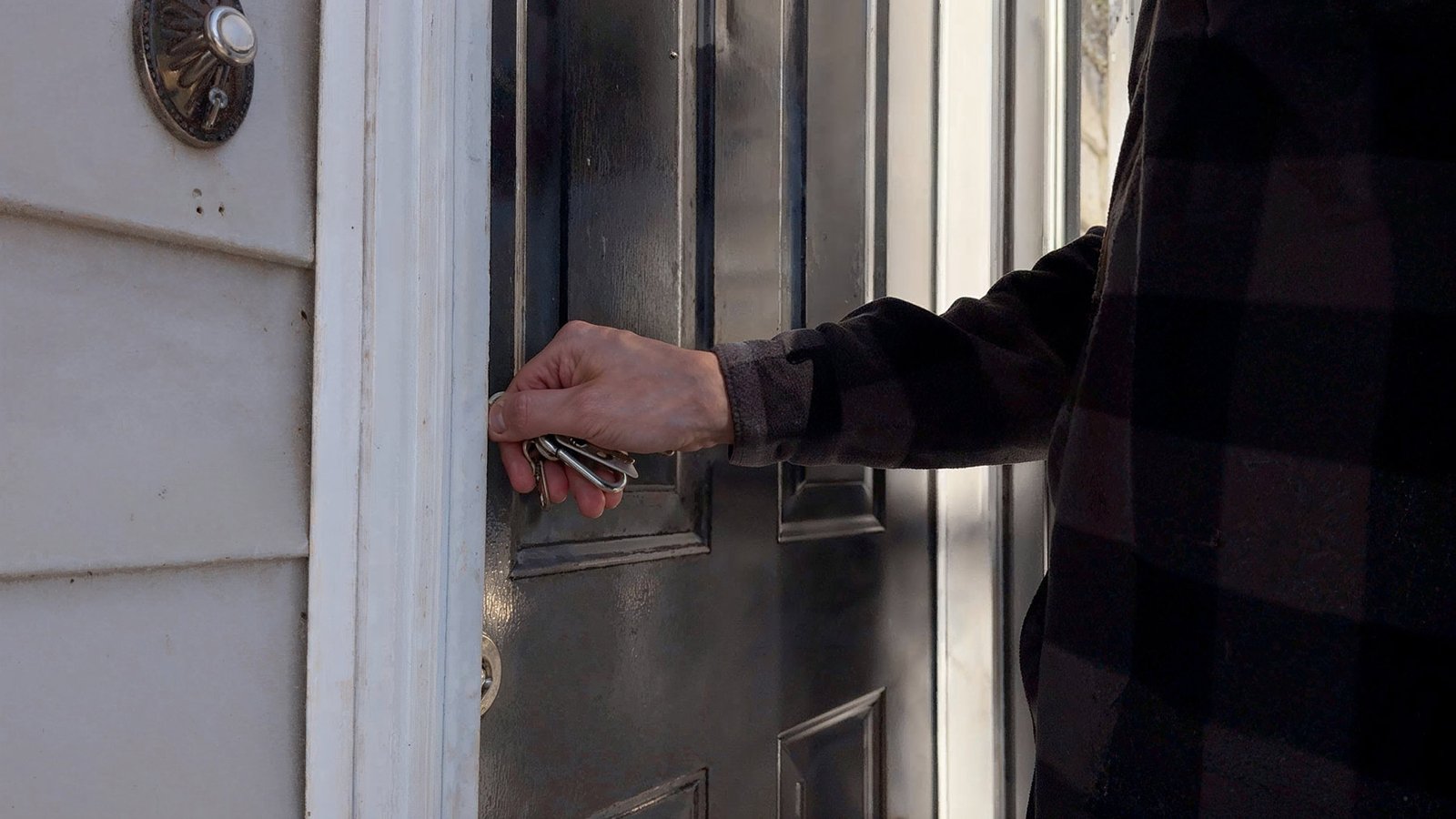 Close-up of a person's hand in a plaid jacket holding keys to unlock a house door, with a focus on security and home access.